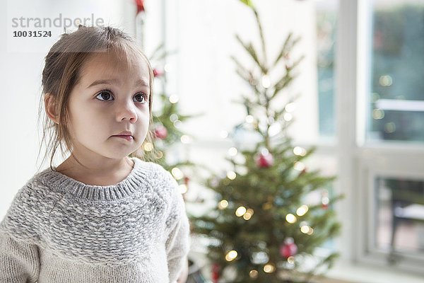 Großäugiges Mädchen  das vor dem Weihnachtsbaum aufblickt