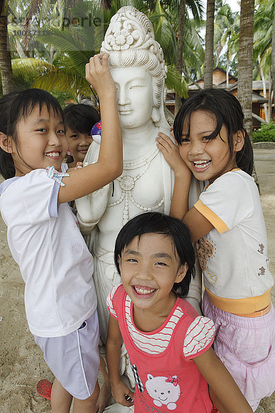 Chinesische lachende Mädchen an einer Buddha Statue am Strand von Dongjiao Yelin  Provinz Hainan  China  Asien