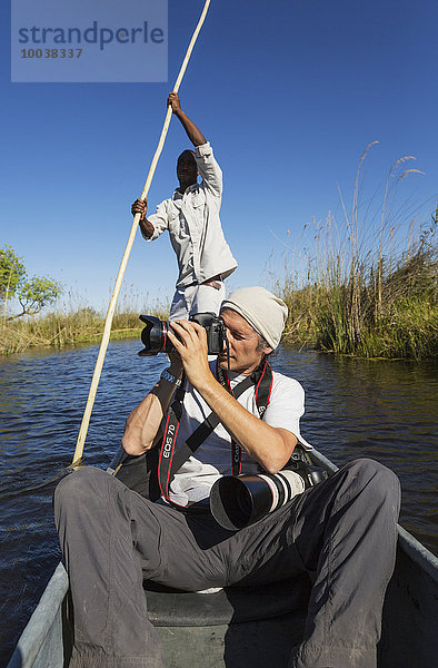 Wildbeobachtung  Fotosafari  Fotograf in einem traditionellen Mokoro Boot  Okavango Delta  Moremi Wildreservat  Botswana  Afrika