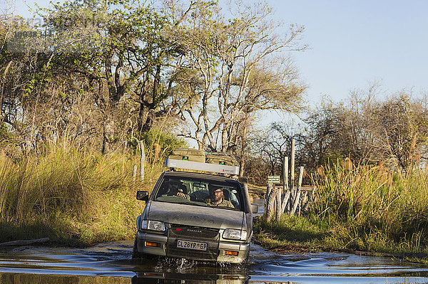 Ein Allradfahrzeug durchquert einen Fluss  Straße im Okavango Delta führt über die Pfahlbrücke Third Bridge  Moremi Wildreservat  Botswana  Afrika