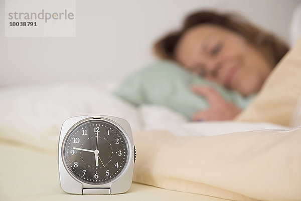 Woman asleep in bed while her alarm shows the early time at home in bedroom  Munich  Bavaria  Germany