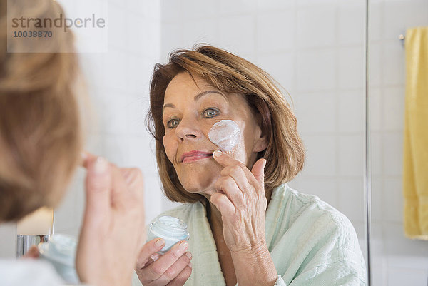 Reflection of a senior woman applying moisturizer on her face in mirror  Munich  Bavaria  Germany