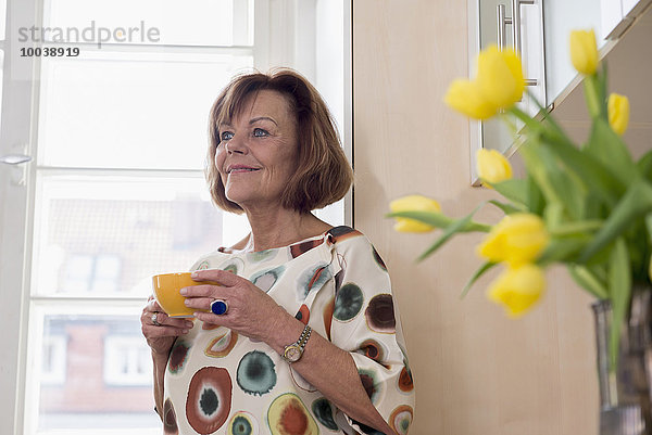 Senior woman dreaming while drinking tea in kitchen Munich  Bavaria  Germany