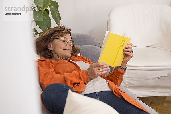 Senior woman reading a book while lying on sofa at home  Munich  Bavaria  Germany