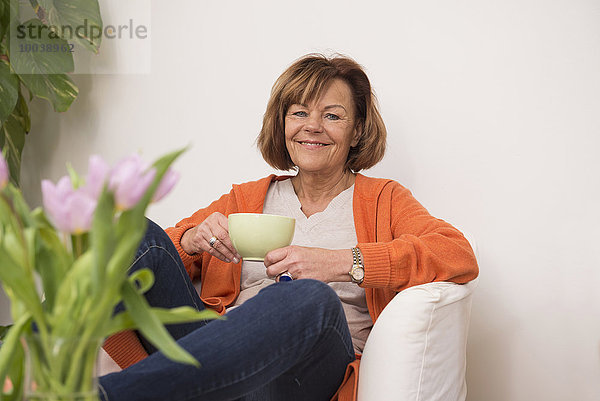 Happy senior woman sitting on sofa and having cup of tea at home  Munich  Bavaria  Germany