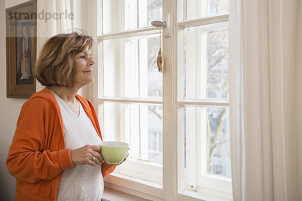 Side profile of a senior woman having cup of tea looking through window at home  Munich  Bavaria  Germany