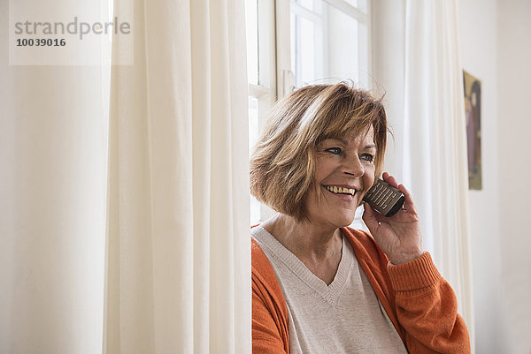 Happy senior woman talking on cell phone at home  Munich  Bavaria  Germany