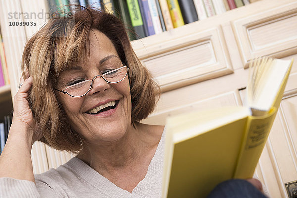 Senior woman while reading in front of bookshelf  Munich  Bavaria  Germany