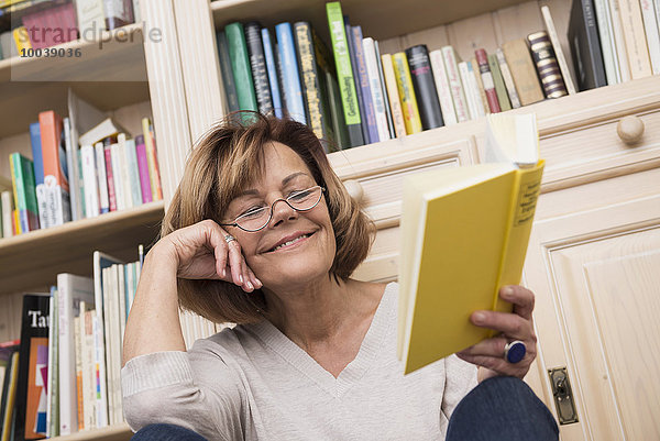 Senior woman sitting in front of bookshelf and reading  Munich  Bavaria  Germany