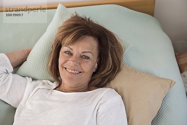 Portrait of senior woman lying on bed and smiling  Munich  Bavaria  Germany