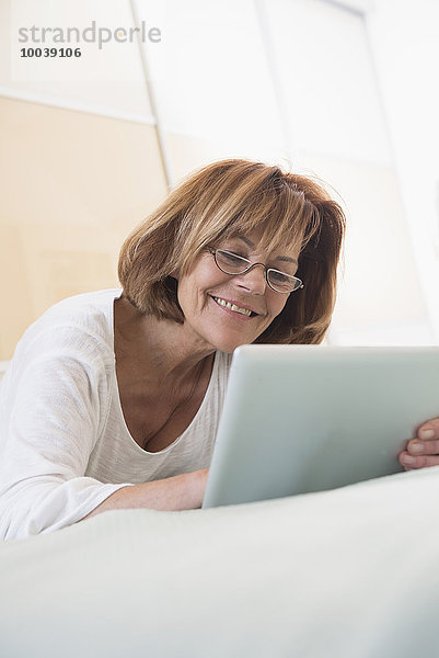 Senior woman lying on bed and using a digital tablet  Munich  Bavaria  Germany