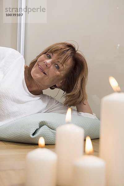 Senior woman lying with pillow on the floor  burning candles in foreground  Munich  Bavaria  Germany