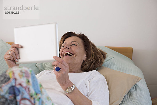 Senior woman lying on bed and using a digital tablet  Munich  Bavaria  Germany