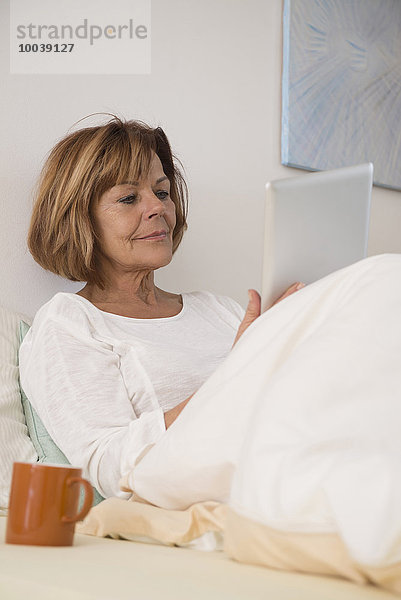 Senior woman sitting on bed and using a digital tablet  Munich  Bavaria  Germany