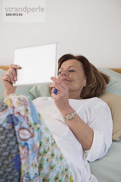 Senior woman lying on bed and using a digital tablet  Munich  Bavaria  Germany