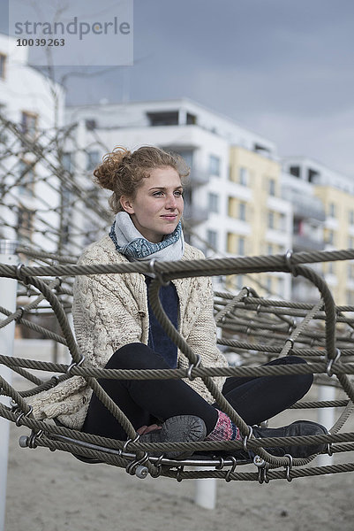 Young woman sitting on climbing net in playground  Munich  Bavaria  Germany