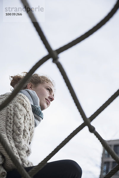 Low angle view of a young woman sitting on climbing net  Munich  Bavaria  Germany