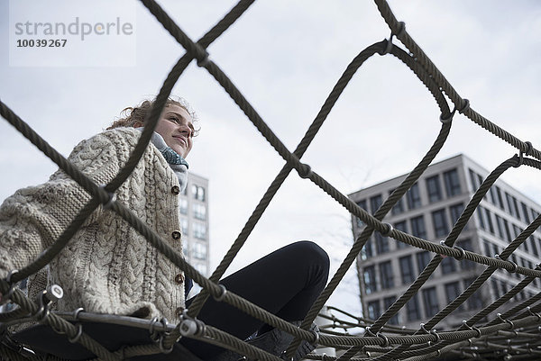 Low angle view of a young woman sitting on climbing net  Munich  Bavaria  Germany