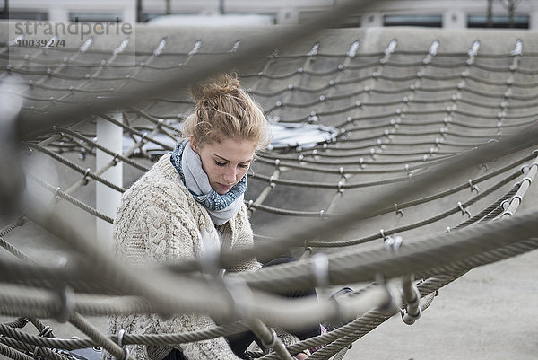 Young woman sitting on climbing net in playground  Munich  Bavaria  Germany