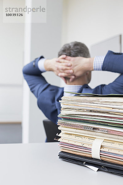 Stack of documents with businessman relaxing in the background  Leipzig  Saxony  Germany