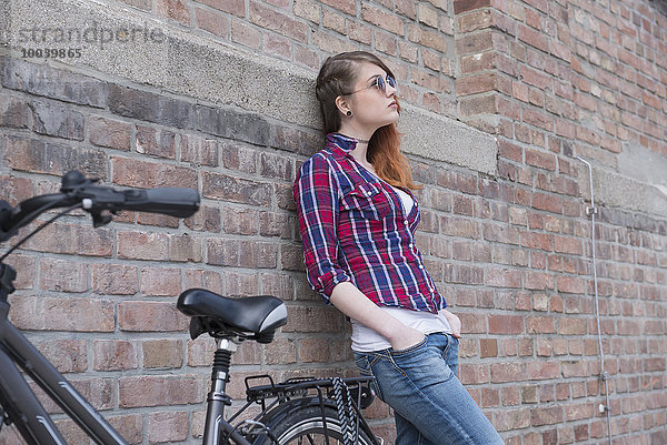 Young woman leaning on wall with bicycle  Munich  Bavaria  Germany