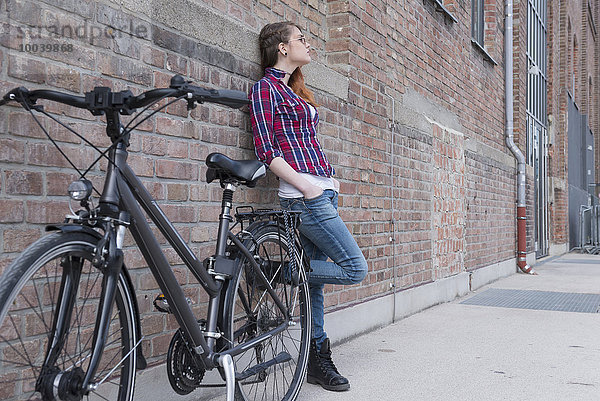 Young woman leaning on wall with bicycle  Munich  Bavaria  Germany