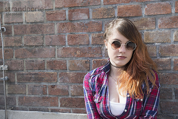 Young woman leaning in front of brick wall  Munich  Bavaria  Germany