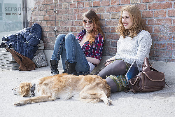 Two friends with dog in front of brick wall  Munich  Bavaria  Germany