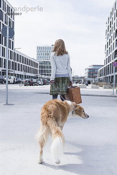 Rear view of woman walking on road with dog and suitcase  Munich  Bavaria  Germany