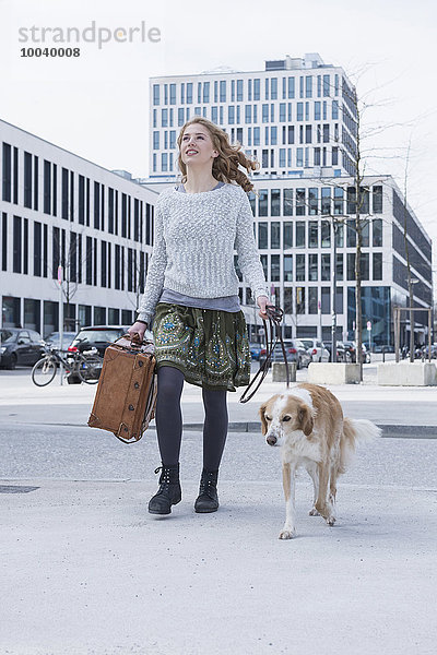 Young woman walking on road with dog and suitcase  Munich  Bavaria  Germany