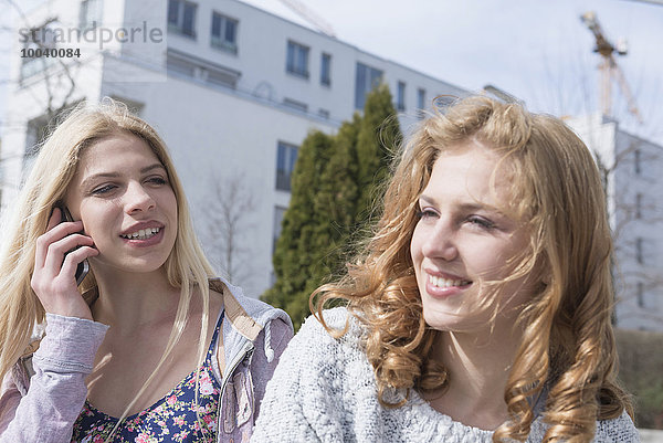 Teenage girl with her friend talking on mobile phone  Munich  Bavaria  Germany