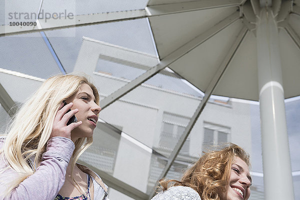 Teenage girl with her friend talking on mobile phone  Munich  Bavaria  Germany