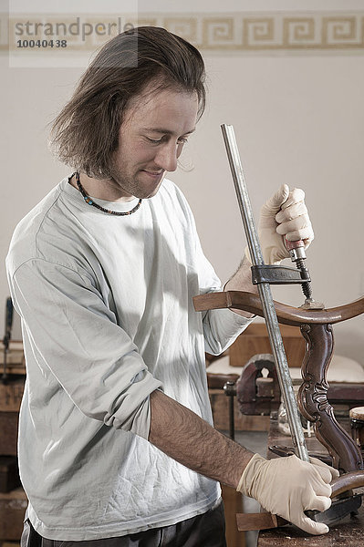 Carpenter fastening a vise to an antique wooden chair at workshop  Bavaria  Germany