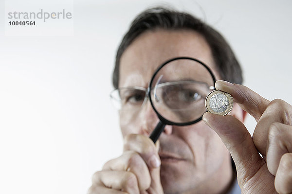 Businessman examining one euro coin with magnifying glass  Bavaria  Germany