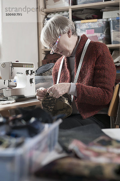 Senior female fashion designer stitching cap in workshop  Bavaria  Germany