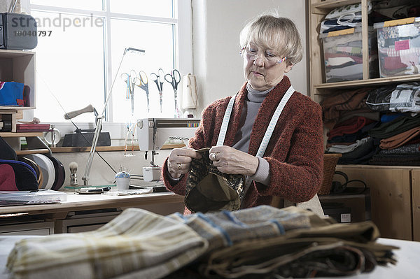 Senior female fashion designer stitching cap in workshop  Bavaria  Germany