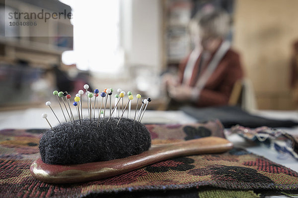 Close-up of pin cushion with senior female fashion designer working in workshop  Bavaria  Germany