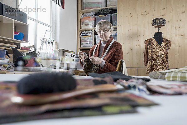 Senior female fashion designer stitching cap in workshop  Bavaria  Germany