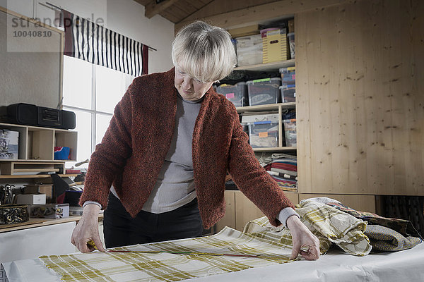 Senior female fashion designer measuring fabric in workshop  Bavaria  Germany