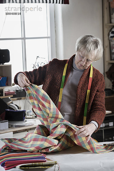 Senior female fashion designer checking fabric in workshop  Bavaria  Germany