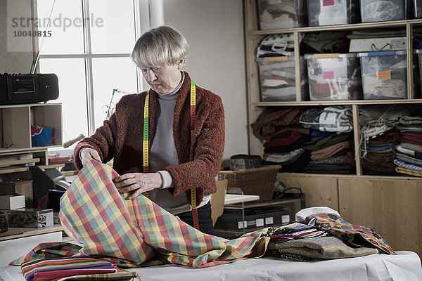 Senior female fashion designer checking fabric in workshop  Bavaria  Germany