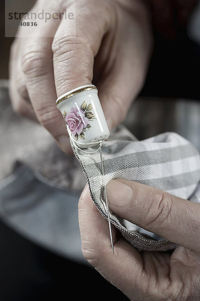 Senior female fashion designer wearing a thimble stitching in workshop  Bavaria  Germany