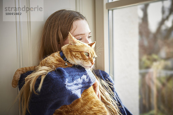 Teenagerin mit Katze durchs Fenster schauend