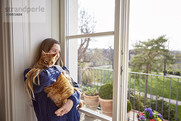 Teenagerin mit Katze durchs Fenster schauend