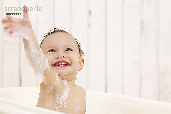 Fröhliches kleines Mädchen mit ausgestrecktem Arm beim Baden in der Badewanne