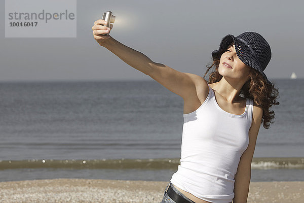 Niederlande  Scheveningen  junge Frau mit einem Selfie am Strand