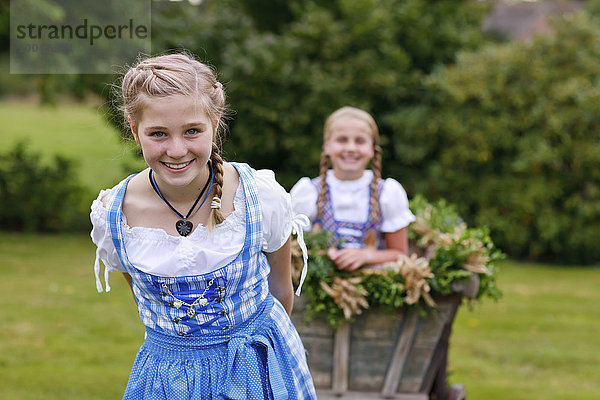 Deutschland  Lüneburger Heide  Porträt eines lächelnden blonden Mädchens im Dirndl  das den Erntewagen zieht