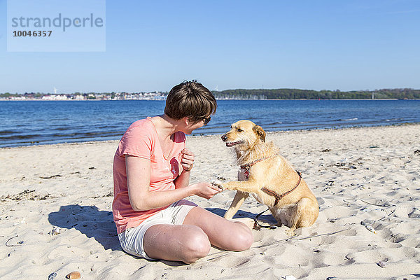 Deutschland  Kiel  Frau sitzend mit ihrem Hund am Sandstrand