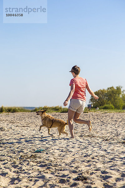 Deutschland  Kiel  Frau läuft mit ihrem Hund am Sandstrand