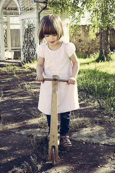 Kleines Mädchen mit altem Holzroller im Garten